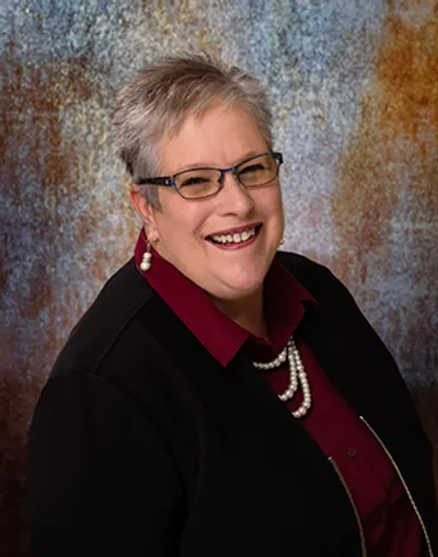 A woman with short hair and glasses is smiling.