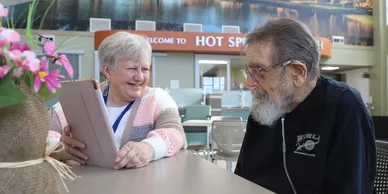 A man and woman sitting at a table with a laptop.