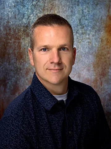 A man in blue shirt and white shirt standing next to wall.