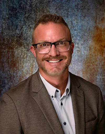 A man in glasses and a suit smiling for the camera.