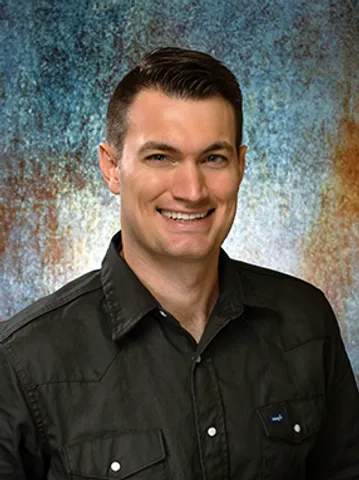 A man smiling for the camera in front of a wall.