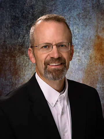 A man with a beard and glasses in a suit.