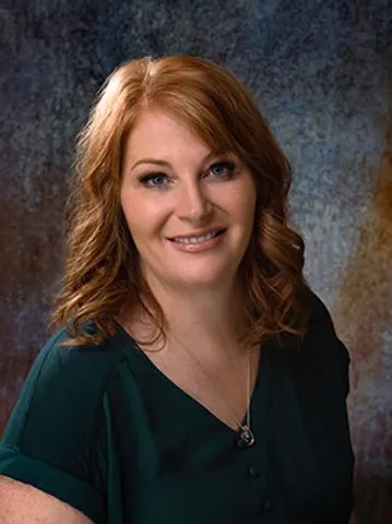 A woman with red hair and wearing green is smiling.