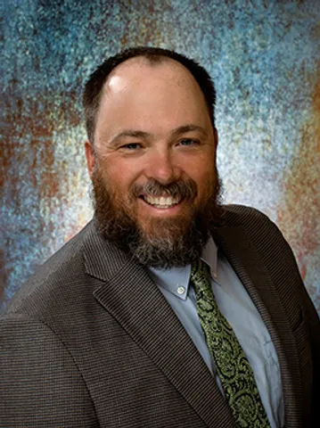 A man with a beard and suit smiling for the camera.